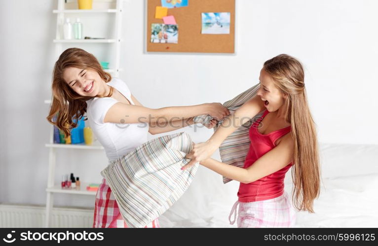 friendship, people and pajama party concept - happy friends or teenage girls having fun and pillow fight on bed at home