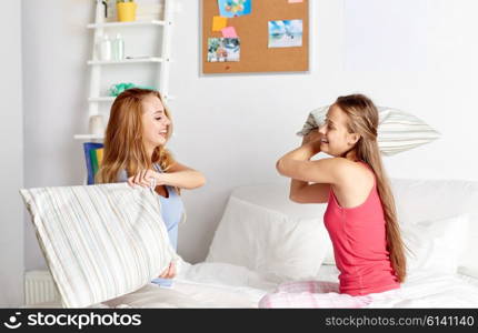 friendship, people and pajama party concept - happy friends or teenage girls having fun and pillow fight on bed at home