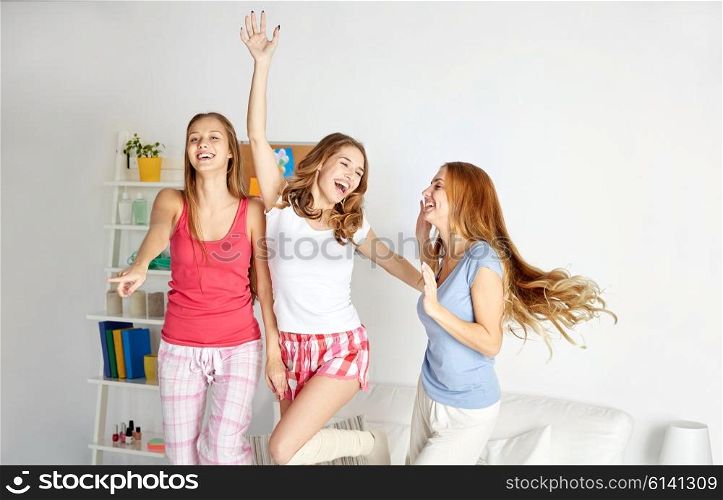 friendship, people and pajama party concept - happy friends or teenage girls having fun, dancing and jumping on bed at home