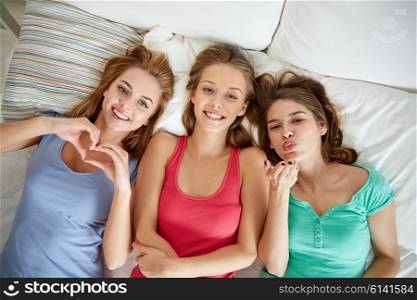 friendship, people and pajama party concept - happy friends or teenage girls having fun and lying in bed at home