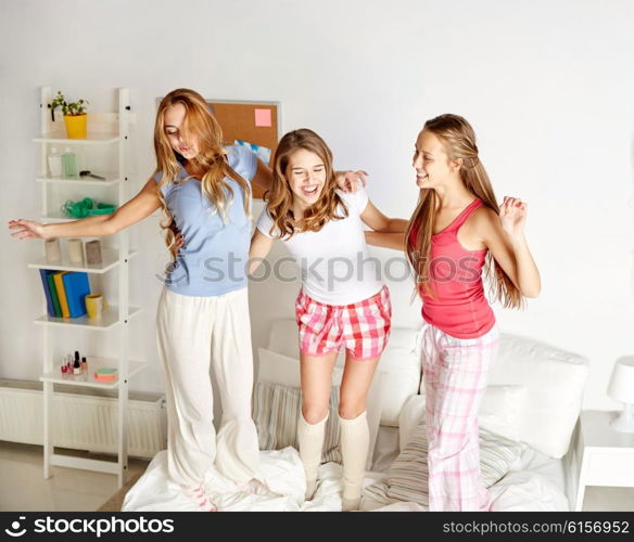 friendship, people and pajama party concept - happy friends or teenage girls having fun, dancing and jumping on bed at home