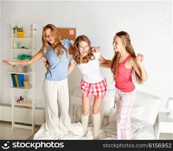 friendship, people and pajama party concept - happy friends or teenage girls having fun, dancing and jumping on bed at home