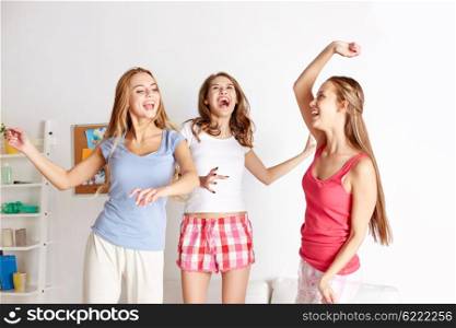 friendship, people and pajama party concept - happy friends or teenage girls having fun and jumping on bed at home