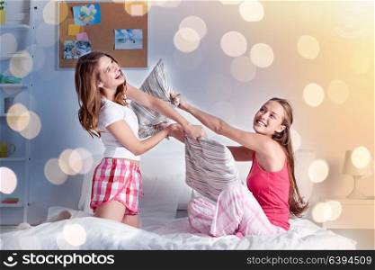 friendship, people and pajama party concept - happy friends or teenage girls having fun and pillow fight on bed at home. happy teen girl friends fighting pillows at home