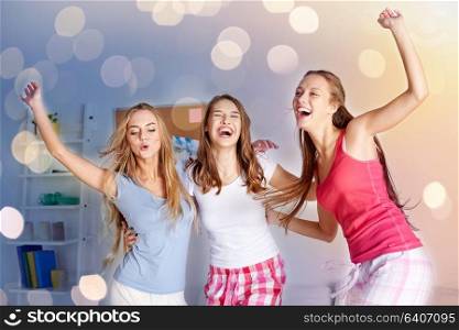 friendship, people and pajama party concept - happy friends or teenage girls having fun and jumping on bed at home. happy friends or teen girls having fun at home