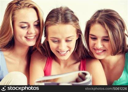 friendship, people and pajama party concept - happy friends or teenage girls reading magazine at home. friends or teen girls reading magazine at home
