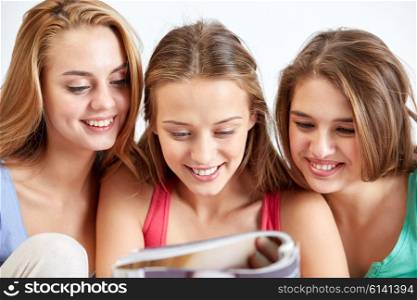 friendship, people and pajama party concept - happy friends or teenage girls reading magazine at home