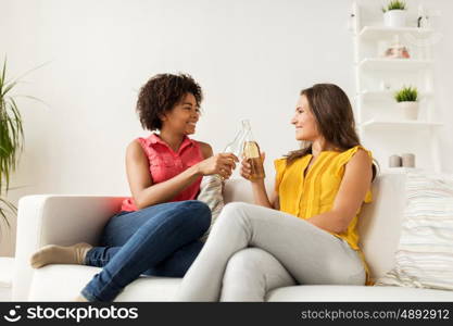 friendship, people, holidays and celebration concept - happy women clinking bottles of beer at home