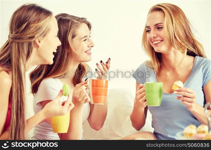 friendship, people, pajama party and communication concept - happy friends or teenage girls drinking, chatting tea and eating sweets at home. happy young women drinking tea with sweets at home