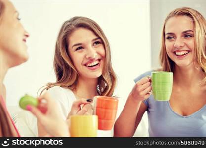 friendship, people, pajama party and communication concept - happy friends or teenage girls drinking, chatting tea and eating sweets at home. happy young women drinking tea with sweets at home