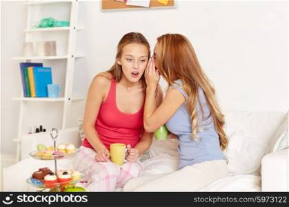 friendship, people, pajama party and communication concept - happy friends or teenage girls drinking tea with sweets and gossiping at home