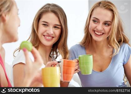 friendship, people, pajama party and communication concept - happy friends or teenage girls drinking, chatting tea and eating sweets at home