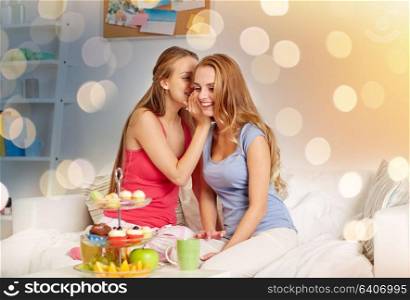 friendship, people, pajama party and communication concept - happy friends or teenage girls drinking tea with sweets and gossiping at home. young women drinking tea and gossiping at home