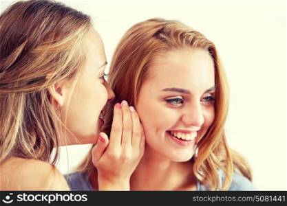 friendship, people, pajama party and communication concept - happy young women gossiping and whispering to ear at home. happy young women whispering gossip at home