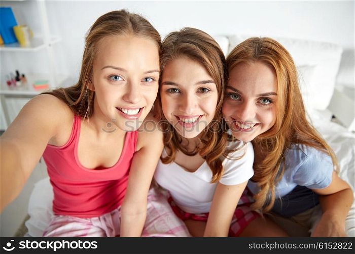 friendship, people, pajama party and fun concept - happy friends or teenage girls taking selfie at home