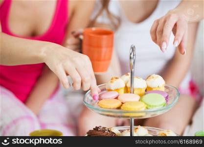 friendship, people, pajama party and junk food concept - close up of friends or teenage girls eating sweets from cake stand at home