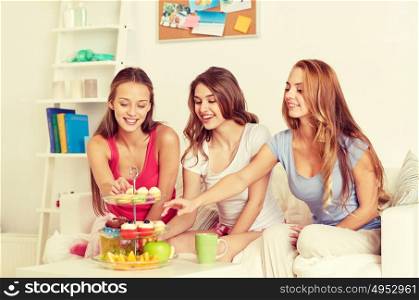 friendship, people, pajama party and junk food concept - happy friends or teenage girls eating sweets at home. happy friends or teen girls eating sweets at home
