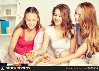 friendship, people, pajama party and junk food concept - happy friends or teenage girls eating pizza at home. happy friends or teen girls eating pizza at home