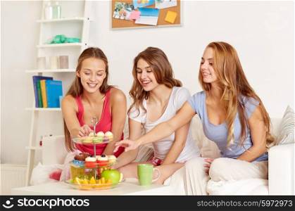 friendship, people, pajama party and junk food concept - happy friends or teenage girls eating sweets at home