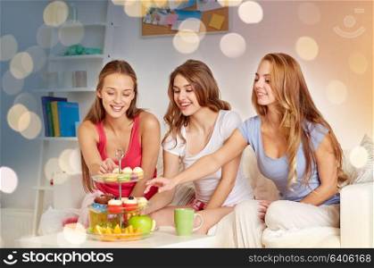friendship, people, pajama party and junk food concept - happy friends or teenage girls eating sweets at home. happy friends or teen girls eating sweets at home