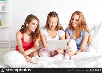 friendship, people, pajama party and technology concept - happy friends or teenage girls with tablet pc computer at home