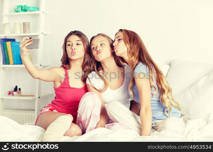 friendship, people, pajama party and technology concept - happy friends or teenage girls with smartphone taking selfie at home. teen girls with smartphone taking selfie at home