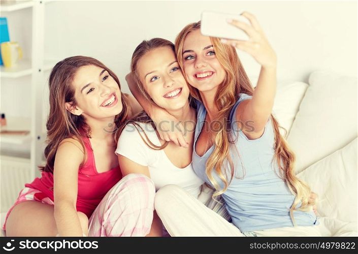 friendship, people, pajama party and technology concept - happy friends or teenage girls with smartphone taking selfie at home. teen girls with smartphone taking selfie at home