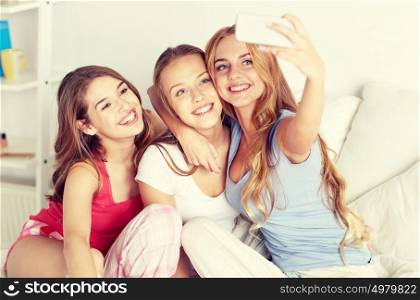 friendship, people, pajama party and technology concept - happy friends or teenage girls with smartphone taking selfie at home. teen girls with smartphone taking selfie at home