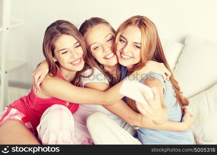 friendship, people, pajama party and technology concept - happy friends or teenage girls with smartphone taking selfie at home. teen girls with smartphone taking selfie at home