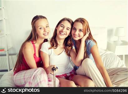 friendship, people, pajama party and technology concept - happy friends or teenage girls with monopod taking selfie at home. teen girls with selfie stick photographing at home. teen girls with selfie stick photographing at home
