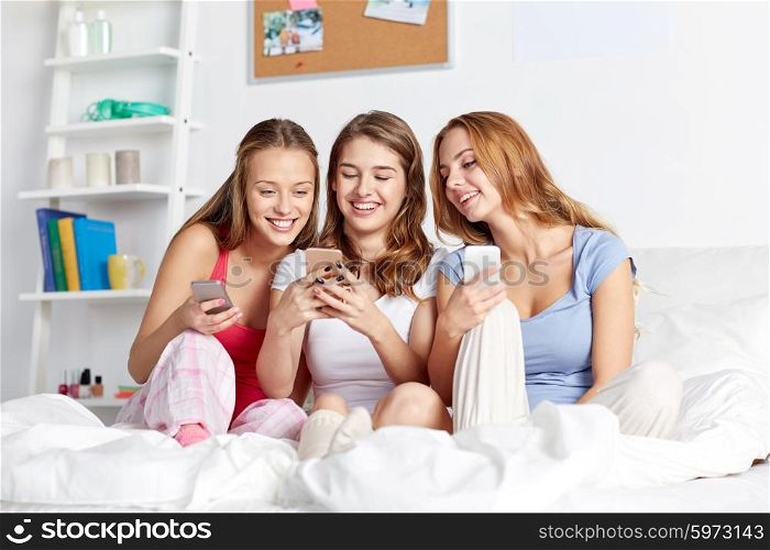 friendship, people, pajama party and technology concept - happy friends or teenage girls with smartphone at home