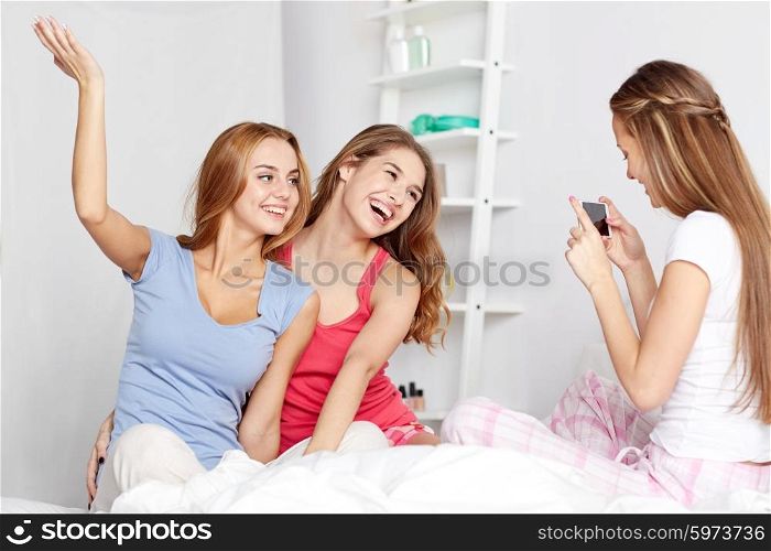 friendship, people, pajama party and technology concept - happy friends or teenage girls with smartphone taking picture at home