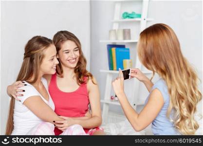 friendship, people, pajama party and technology concept - happy friends or teenage girls with smartphone taking picture at home