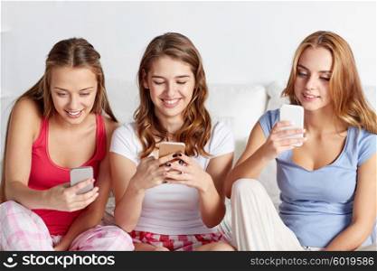 friendship, people, pajama party and technology concept - happy friends or teenage girls with smartphone at home