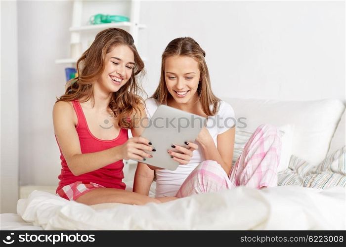 friendship, people, pajama party and technology concept - happy friends or teenage girls with tablet pc computer at home