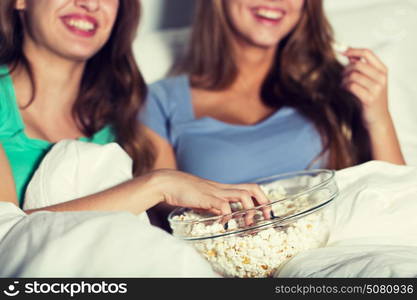 friendship, people, pajama party, entertainment and junk food concept - close up of happy friends or teenage girls eating popcorn and watching movie or tv series at home. happy women eating popcorn and watching tv at home
