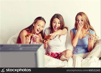 friendship, people, pajama party, entertainment and junk food concept - happy friends or teenage girls eating pizza and watching movie or tv series at home. happy friends eating pizza and watching tv at home