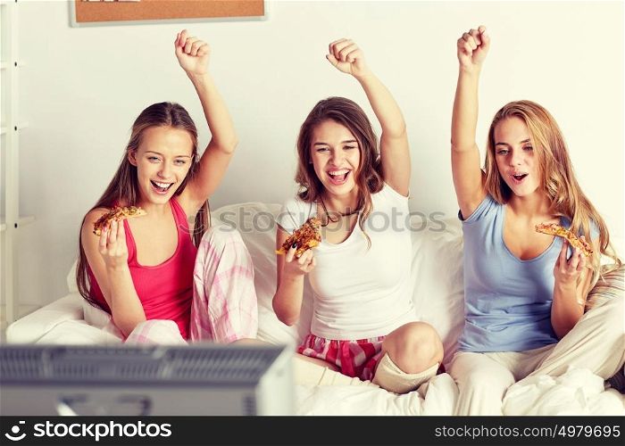 friendship, people, pajama party, entertainment and junk food concept - happy friends or teenage girls eating pizza and watching tv at home. happy friends or teen girls eating pizza at home
