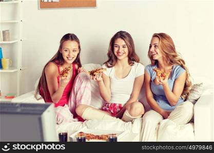 friendship, people, pajama party, entertainment and junk food concept - happy friends or teenage girls eating pizza and watching movie or tv series at home. happy friends eating pizza and watching tv at home