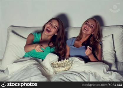 friendship, people, pajama party, entertainment and junk food concept - happy friends or teenage girls eating popcorn and watching movie or tv series at home. happy friends with popcorn and watching tv at home. happy friends with popcorn and watching tv at home