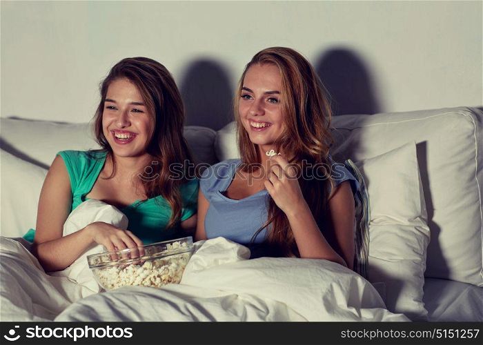 friendship, people, pajama party, entertainment and junk food concept - happy friends or teenage girls eating popcorn and watching movie or tv series at home. happy friends with popcorn and watching tv at home