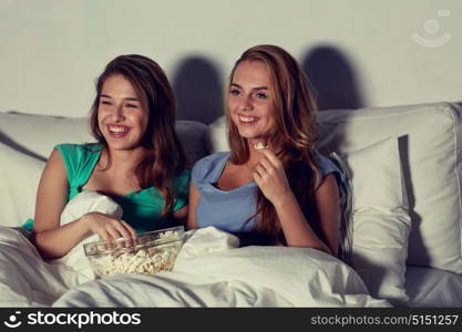 friendship, people, pajama party, entertainment and junk food concept - happy friends or teenage girls eating popcorn and watching movie or tv series at home. happy friends with popcorn and watching tv at home