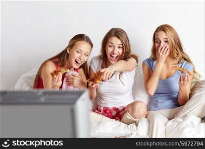 friendship, people, pajama party, entertainment and junk food concept - happy friends or teenage girls eating pizza and watching movie or tv series at home
