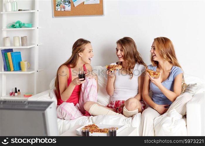 friendship, people, pajama party, entertainment and junk food concept - happy friends or teenage girls eating pizza and watching tv at home