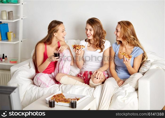 friendship, people, pajama party, entertainment and junk food concept - happy friends or teenage girls eating pizza and watching movie or tv series at home