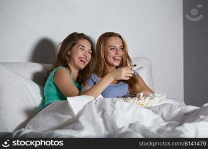 friendship, people, pajama party, entertainment and junk food concept - happy friends or teenage girls eating popcorn and watching movie or tv series at home