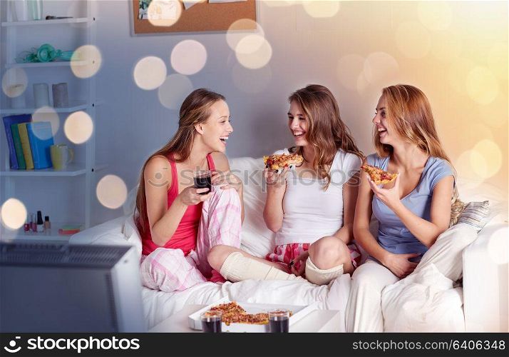 friendship, people, pajama party, entertainment and junk food concept - happy friends or teenage girls eating pizza and watching tv at home. happy friends or teen girls eating pizza at home