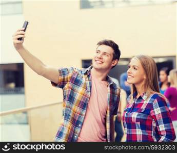 friendship, people, technology and education concept - group of smiling students with smartphone taking selfie outdoors