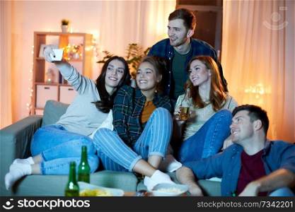 friendship, people, technology and entertainment concept - happy friends with snacks and non-alcoholic drinks taking selfie by smartphone at home in evening. happy friends taking selfie by smartphone at home