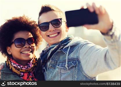 friendship, relations, tourism, travel and people concept - happy teenage friends or couple in sunglasses with smartphone taking selfie outdoors
